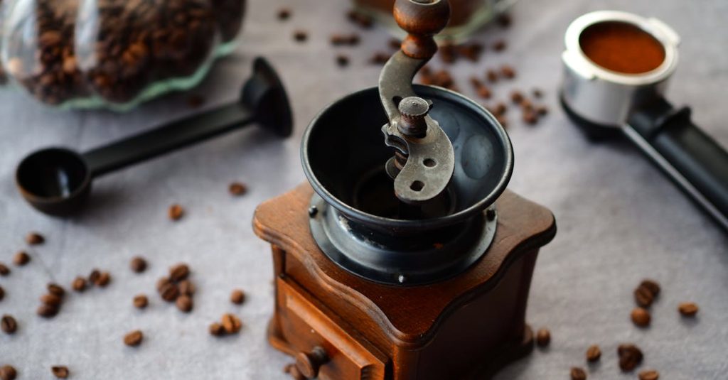 Vintage manual coffee grinder surrounded by scattered coffee beans and tools on a rustic table. how to make coffee at home